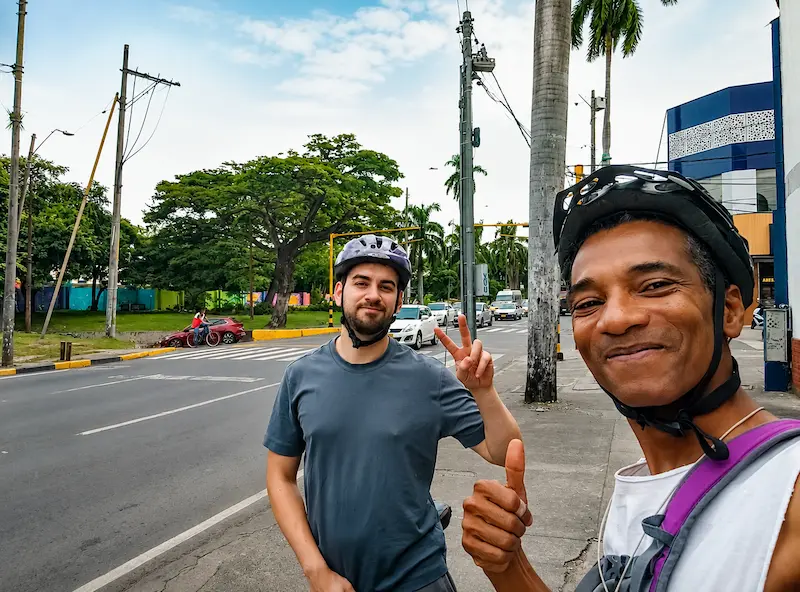 Guía y viajero con cascos de ciclismo posan en una avenida de Cali durante el city tour en bicicleta