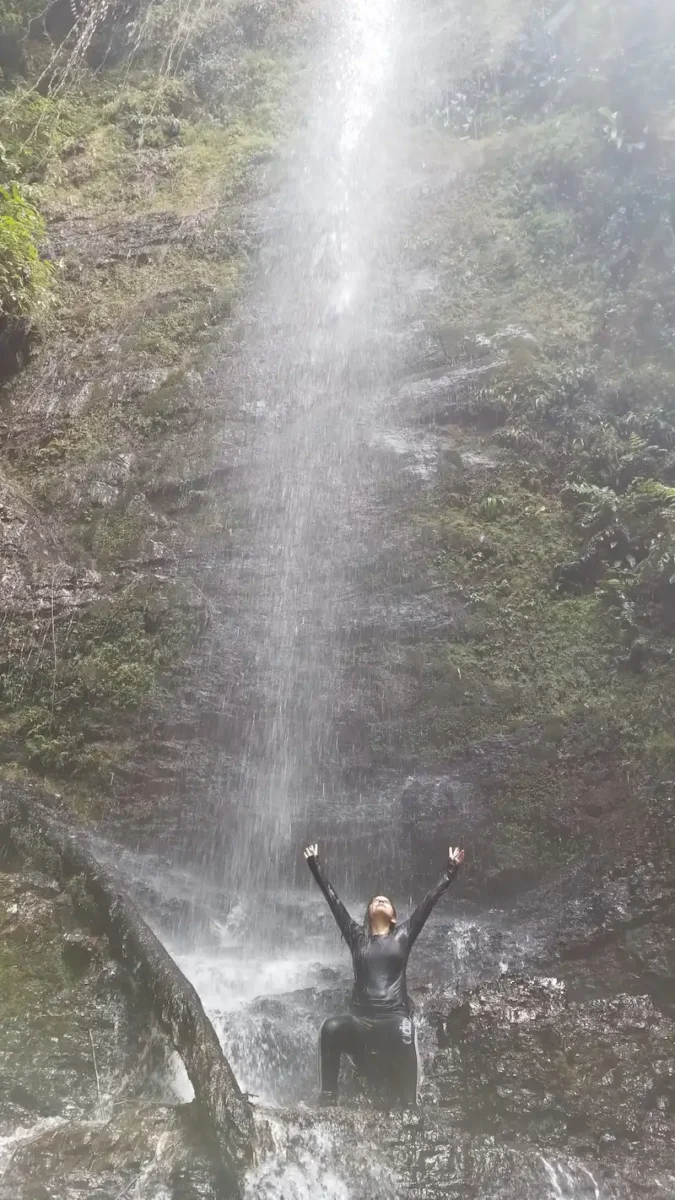 Visitante con los brazos abiertos bajo el rocío de la cascada, en la eco caminata de Pance